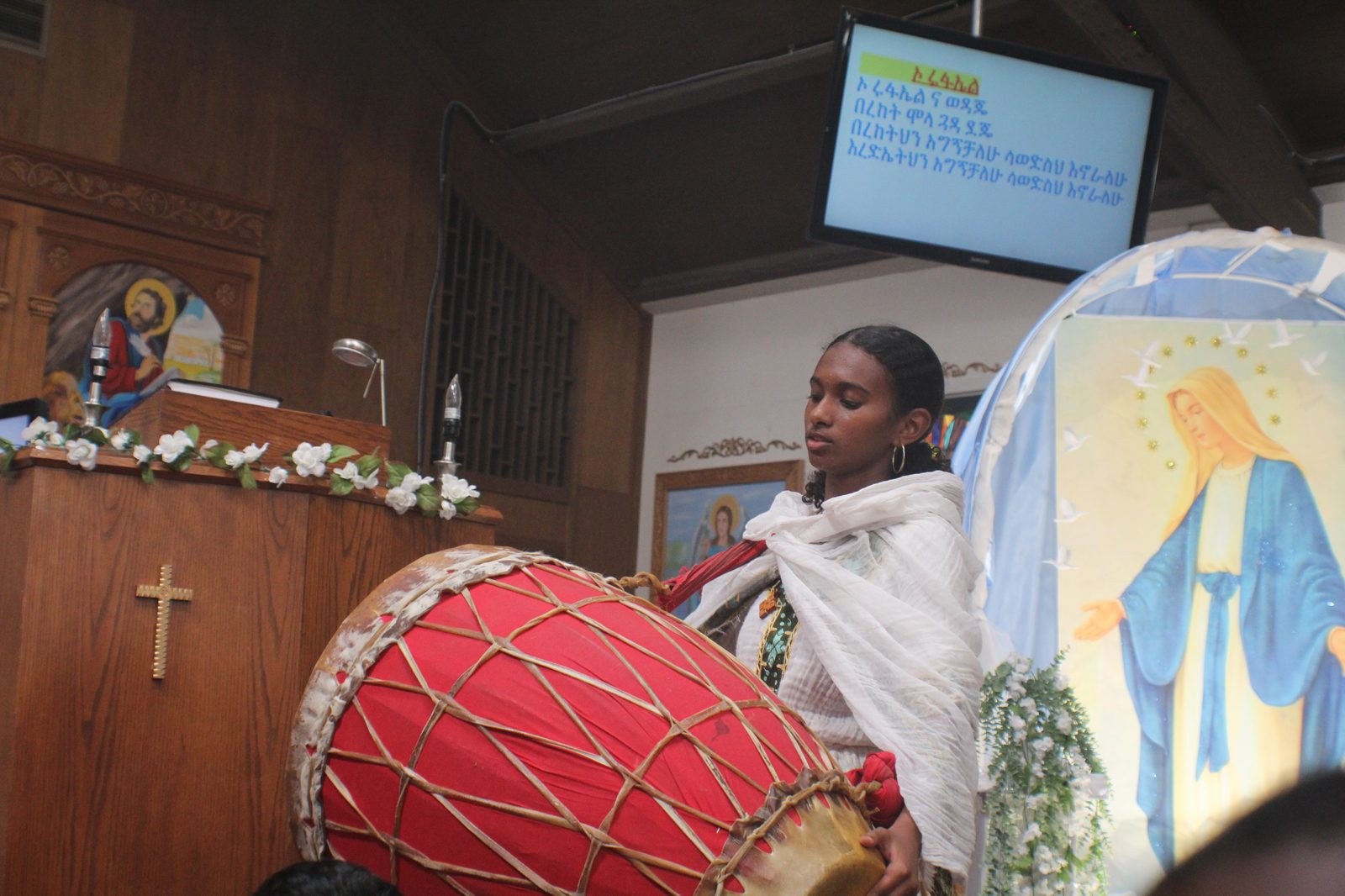 A young woman playing the kebero during mezmur