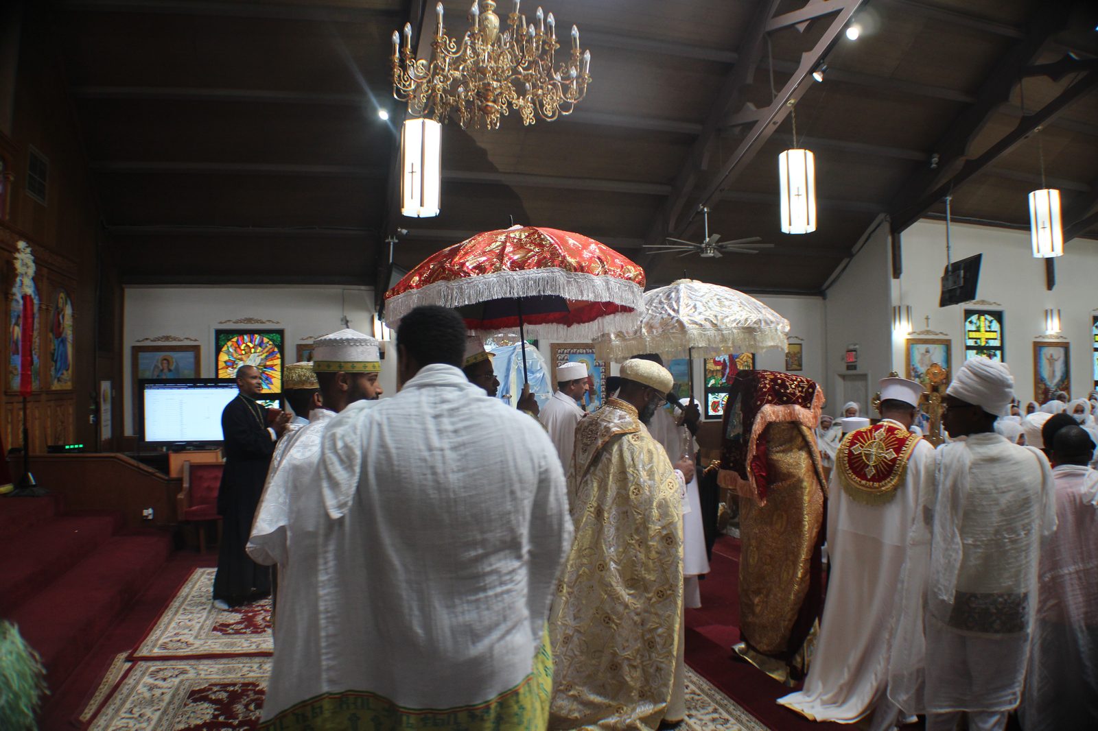 Clergy and faithful in procession beneath ceremonial umbrellas